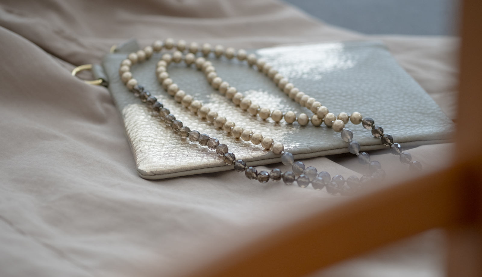 箔座のレザーポーチの上に重ねられた箔珠ネックレス・ロング。お出かけ前の心弾むひととき
