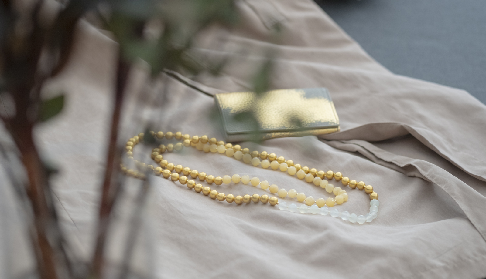 柔らかな光と植物の影の中で美しく佇む、箔座の箔珠ネックレス・ロングとレザー名刺入れ