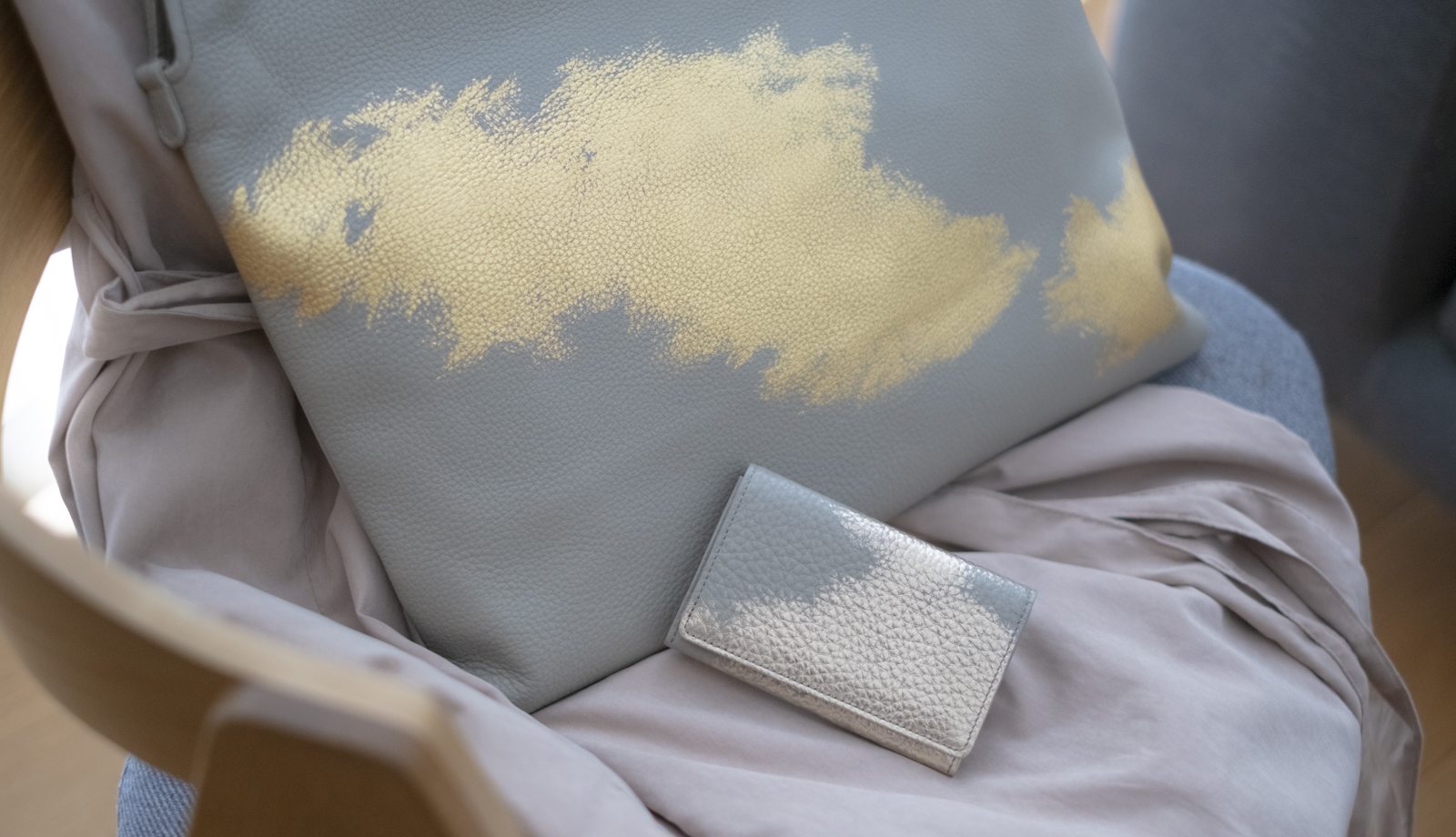 柔らかな光が差し込む部屋の椅子に置かれた、金箔が施されたレザーバッグと名刺入れ