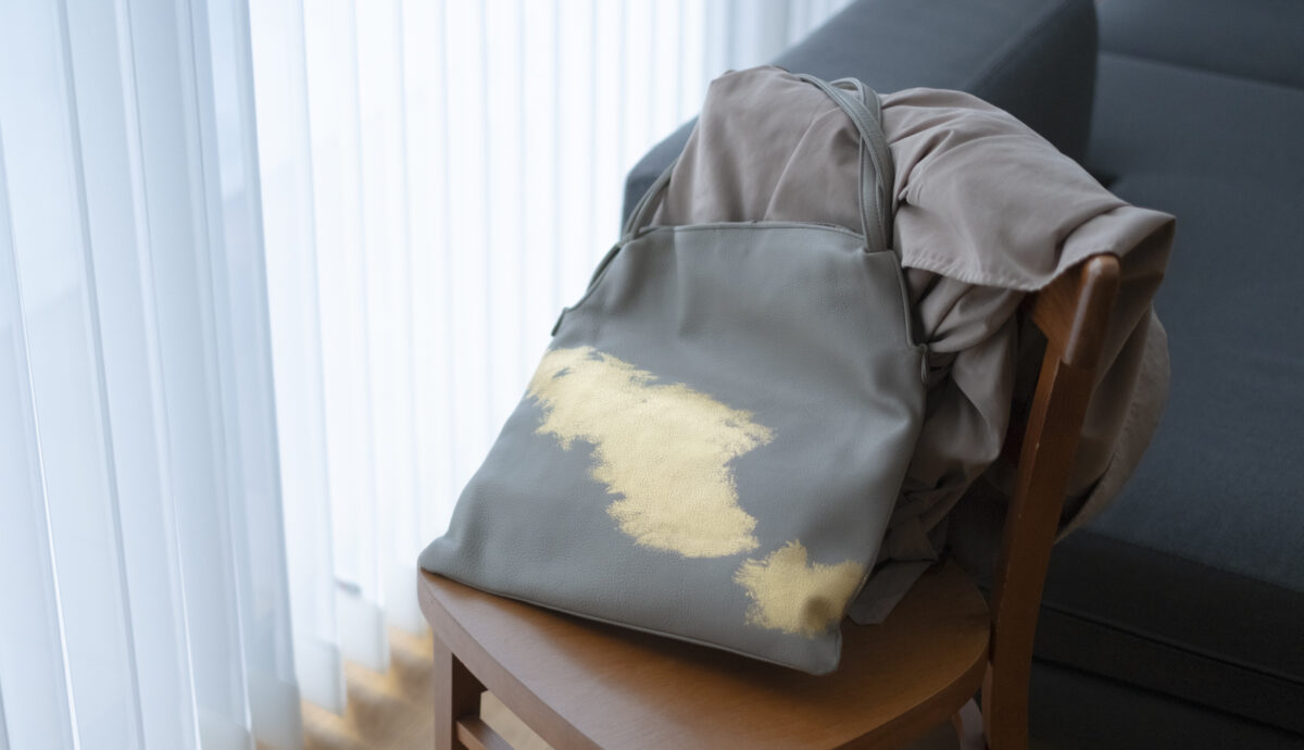 落ち着いたグレーの生地に大胆な金箔のデザインが映える、椅子に掛けられた箔座のレザートートバッグ