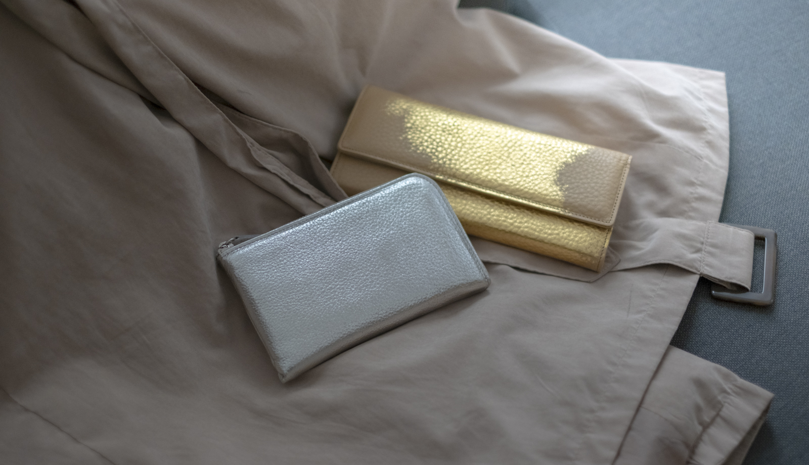 丁寧な暮らしを感じさせるトレンチコートと、寄り添うように置かれた箔座のレザーショート財布とレザー長財布